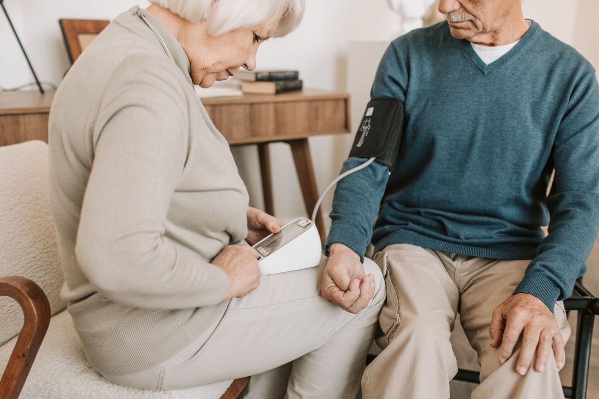 Older woman reading a blood pressure monitor while the man beside her wears the cuff