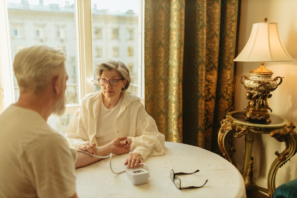 Gray-haired woman with a blood pressure cuff and monitor at a round table
