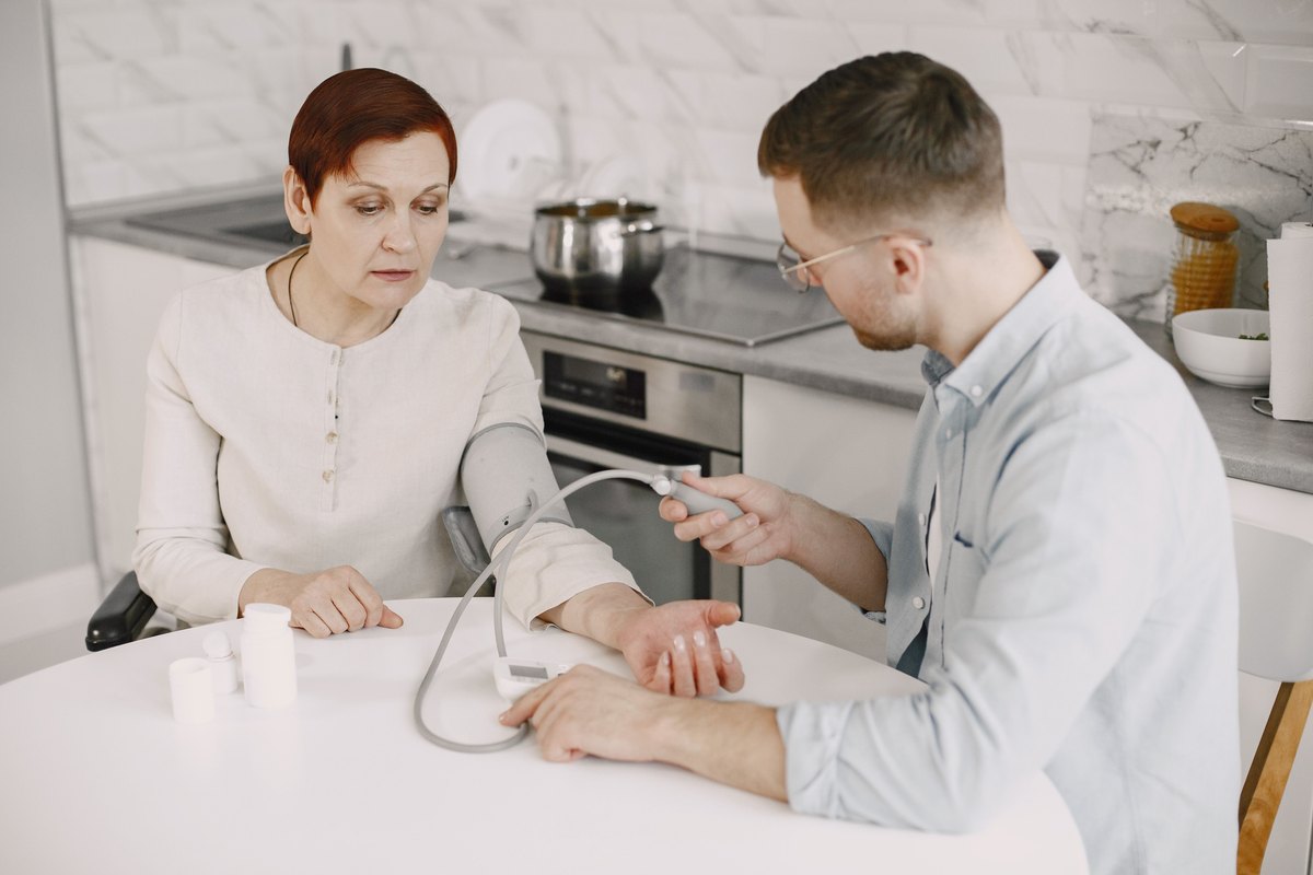 Man checking the blood pressure of a woman at a kitchen table