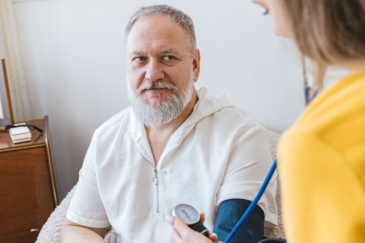 Woman reading a manual gauge while checking a bearded man blood pressure