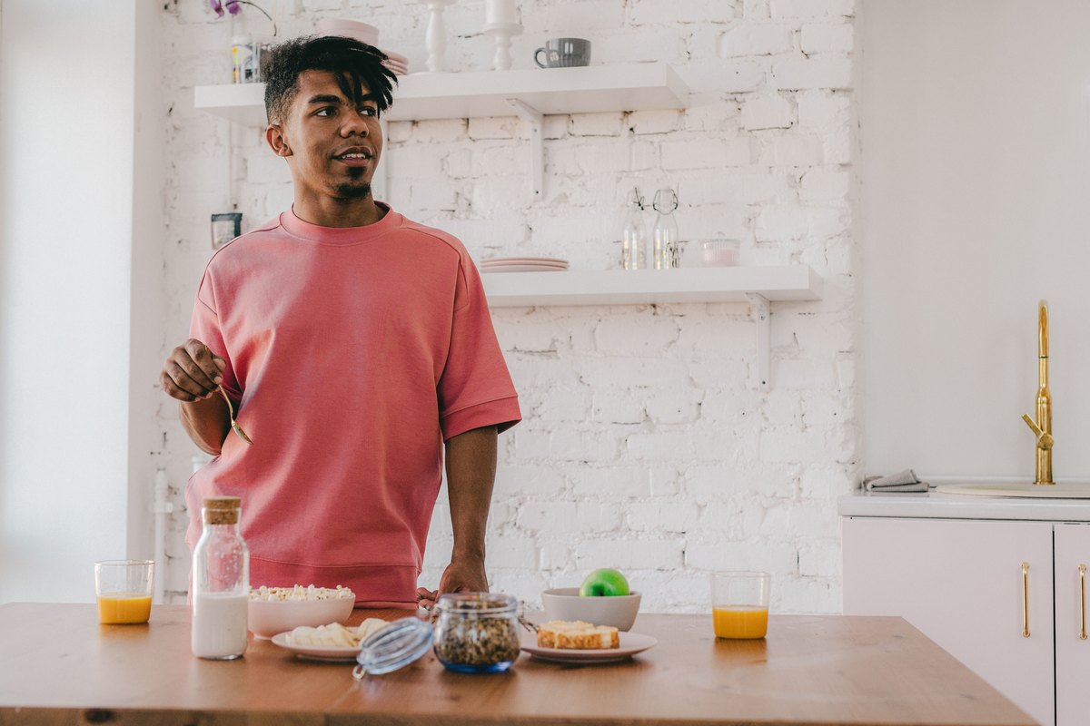 Young man at a kitchen table set with breakfast, milk and fruit