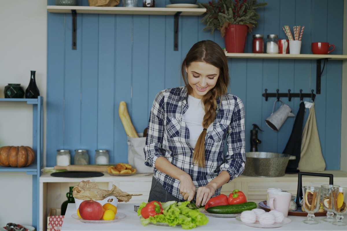Smiling woman chopping vegetables at a kitchen counter full of produce