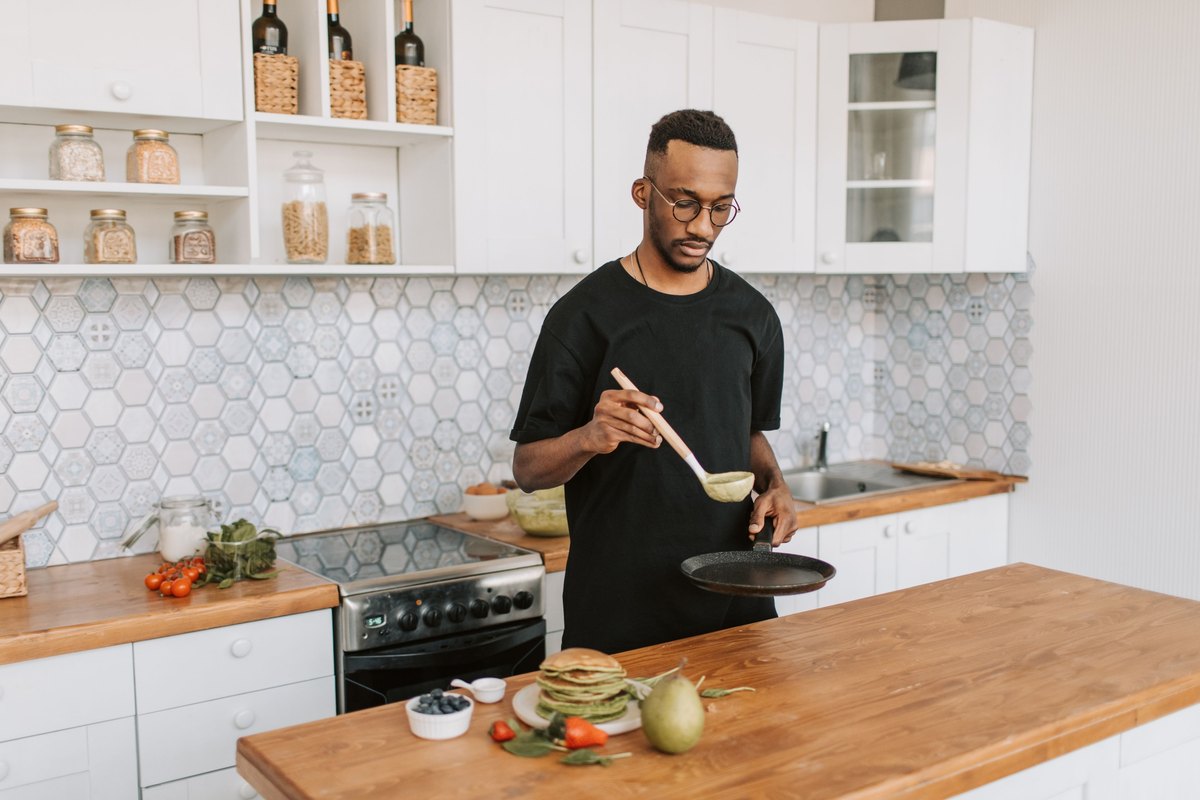 Man in glasses cooking pancakes in a frying pan in a bright kitchen