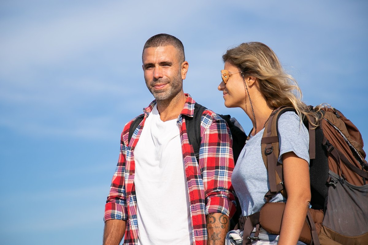 Man and woman with hiking backpacks standing against a blue sky