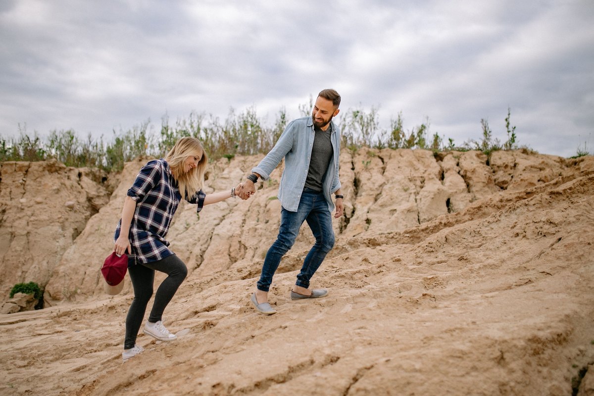 Couple holding hands as they climb a sandy slope