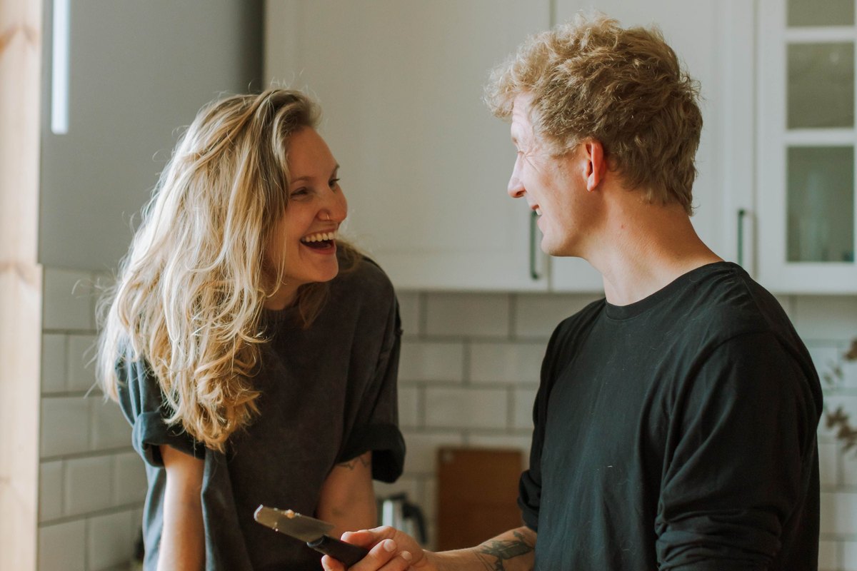Couple laughing together over a pan of crumble in their kitchen