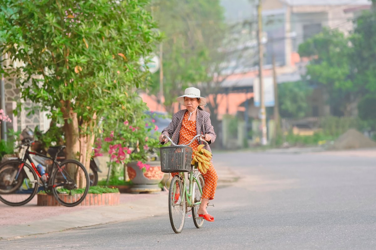 Woman in a sun hat riding a green bicycle with bananas on the handlebars