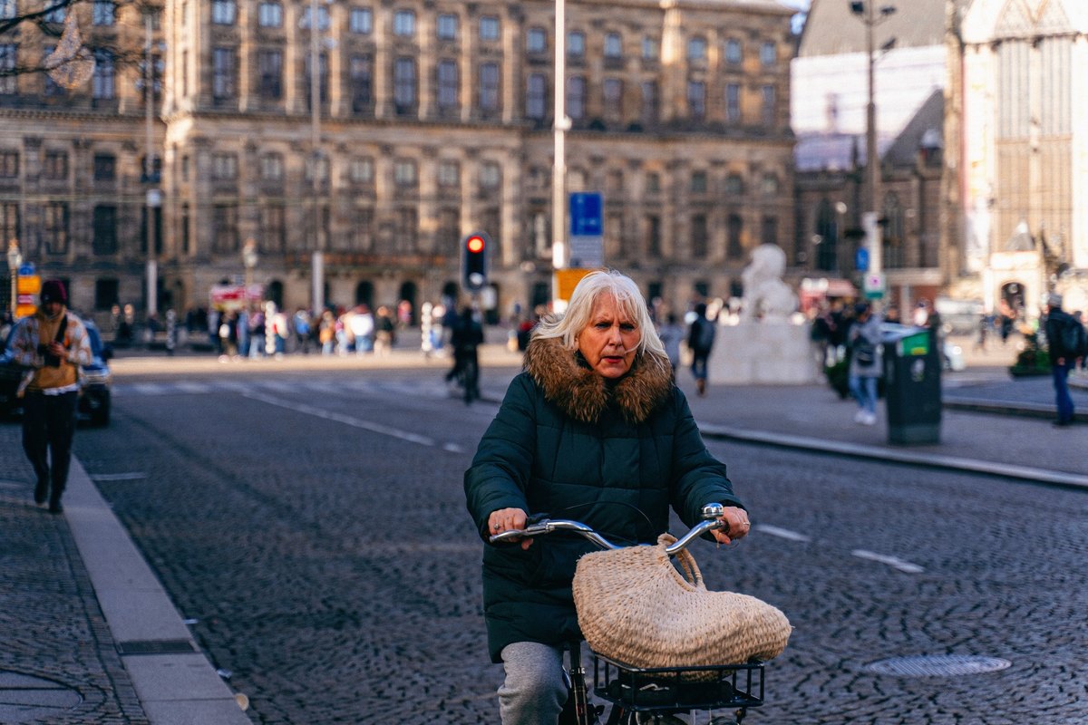 Woman with white-blonde hair riding a bicycle across a cobbled square