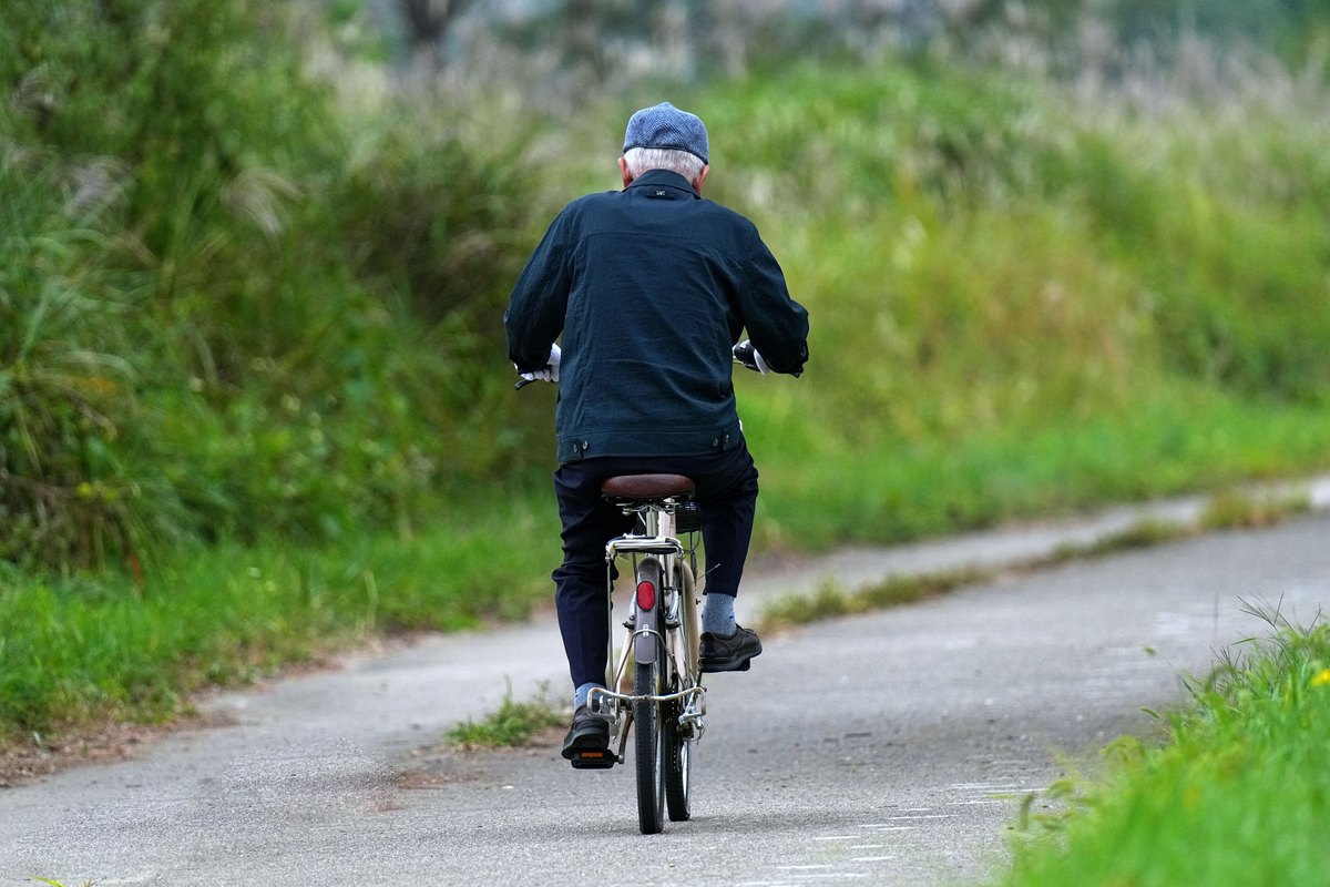 Older man in a flat cap riding a bicycle along a paved path