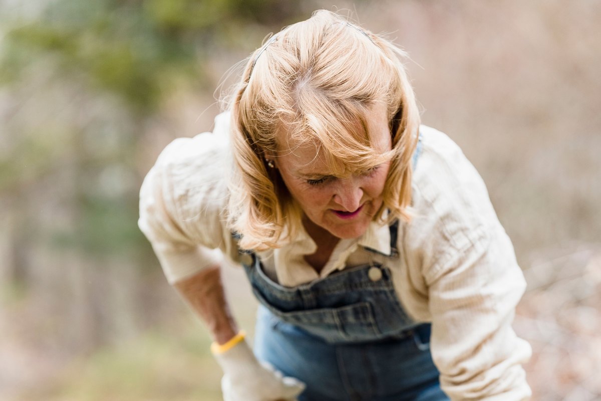 Woman in denim overalls and rubber boots digging with a shovel
