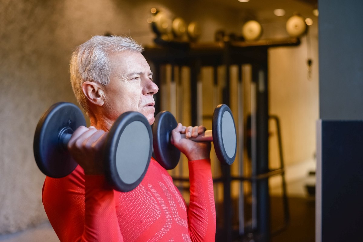 Gray-haired man lifting a pair of dumbbells in a gym