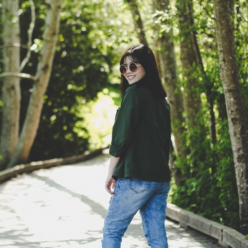 Smiling woman in round sunglasses looking back over her shoulder on a wooded boardwalk