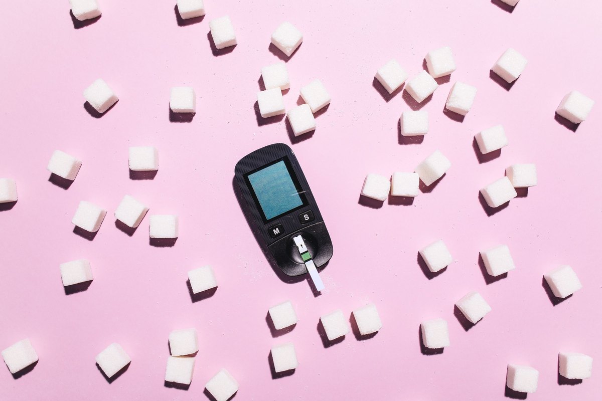 Blood glucose meter with a test strip among white sugar cubes on pink