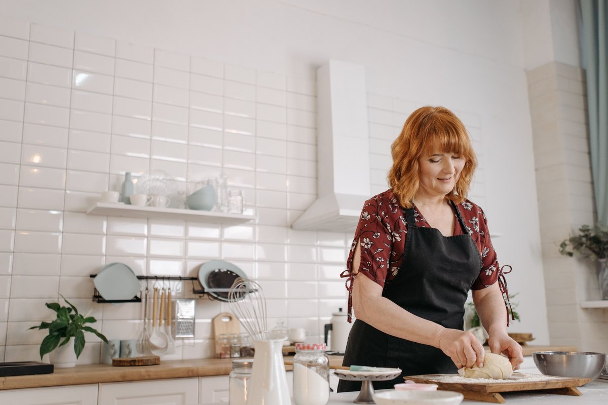 Smiling woman with red hair kneading dough in a white kitchen