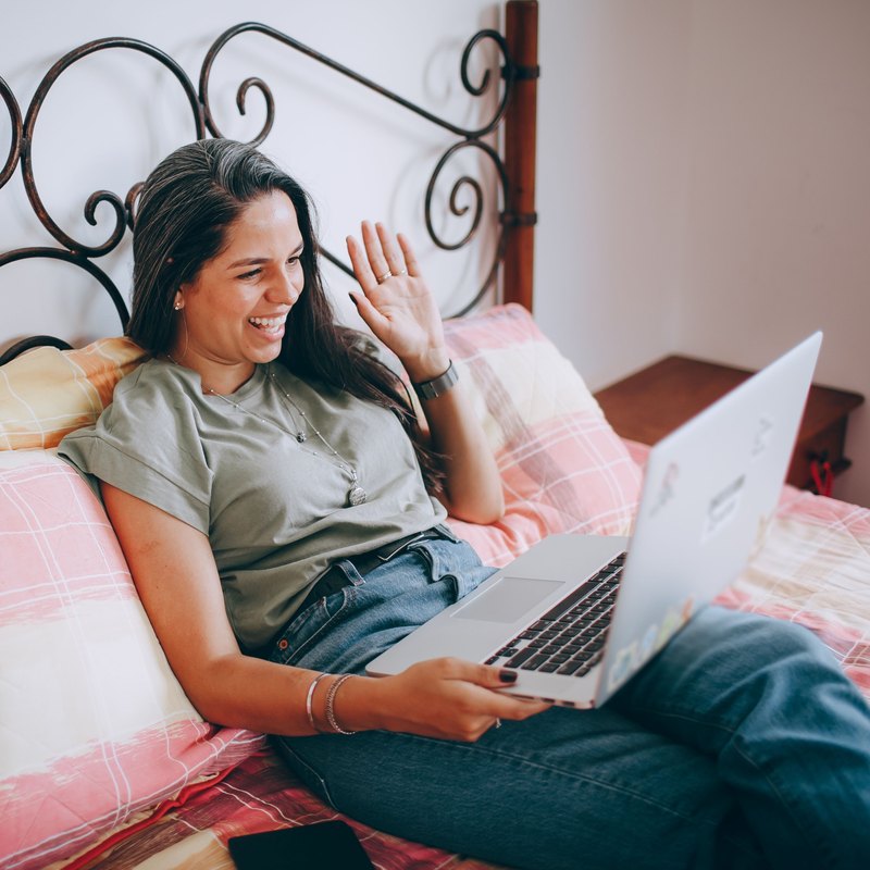 Laughing woman on a bed waving at the laptop on her lap