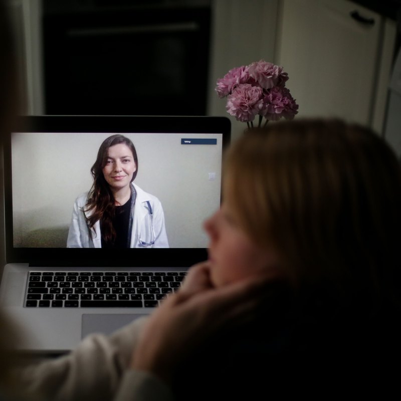 Woman at home watching a clinician in a white coat on a laptop video call
