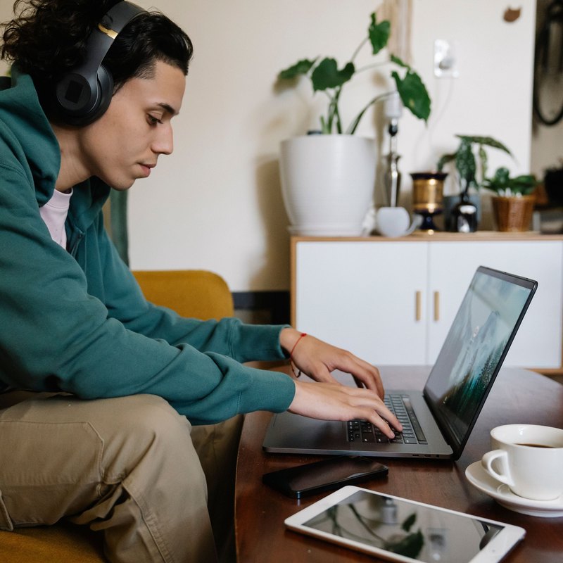 Young man in headphones typing on a laptop at a coffee table