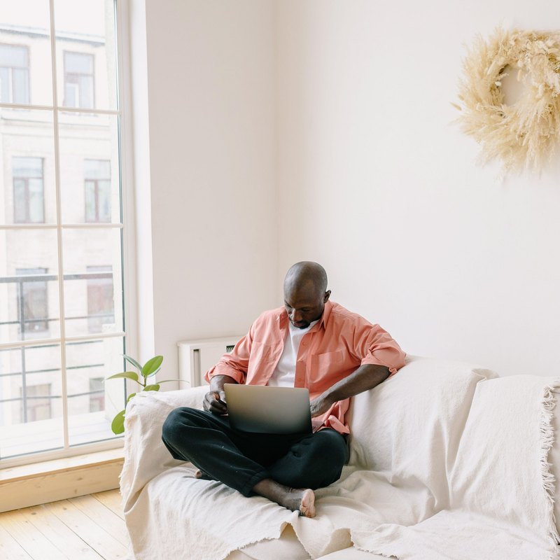 Man sitting cross-legged on a sofa with a laptop on his lap