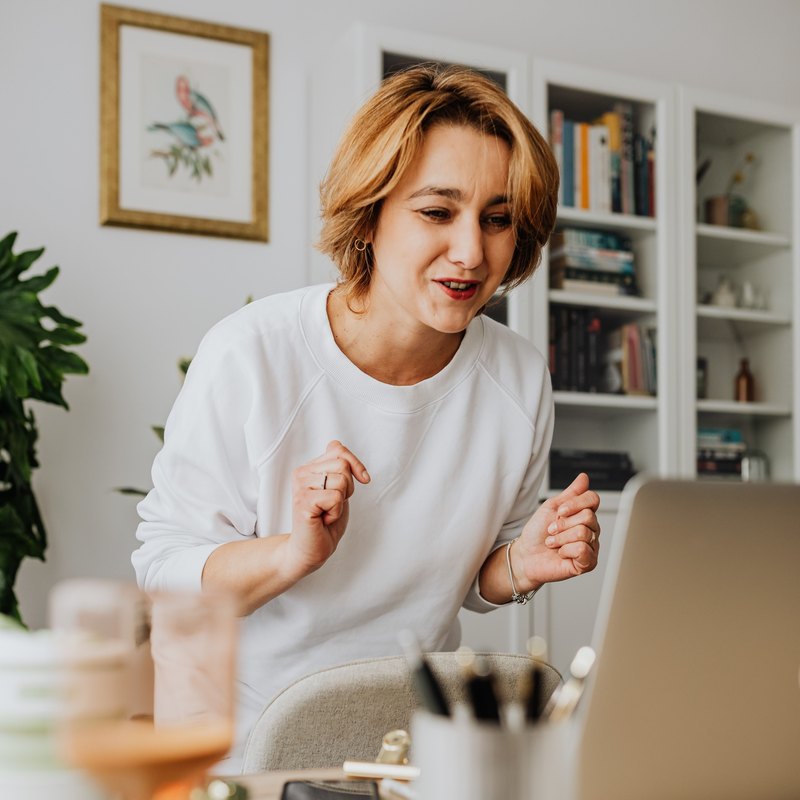 Woman in a white sweatshirt talking toward a laptop at her desk