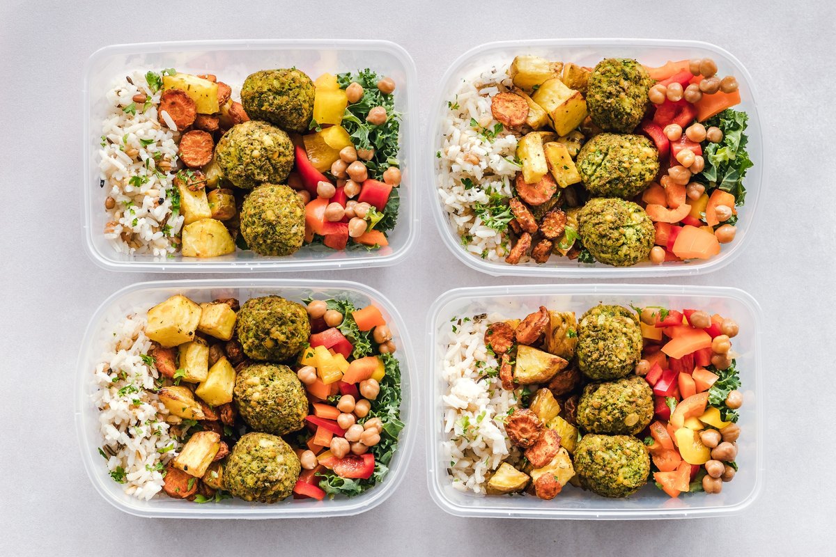 Four meal-prep containers of rice, falafel, roasted vegetables and chickpeas