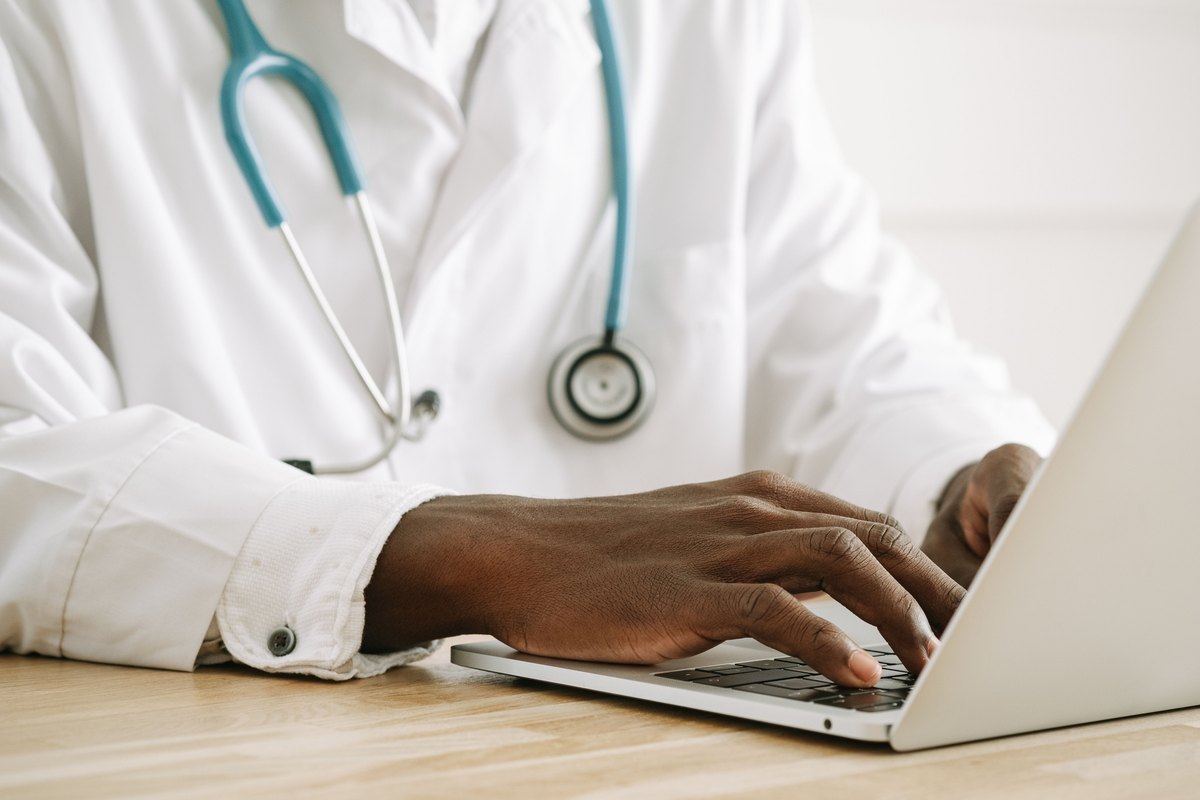 Hands typing on a laptop beside a teal stethoscope