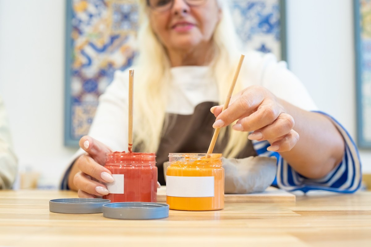 Woman dipping wooden brushes into jars of red and orange paint