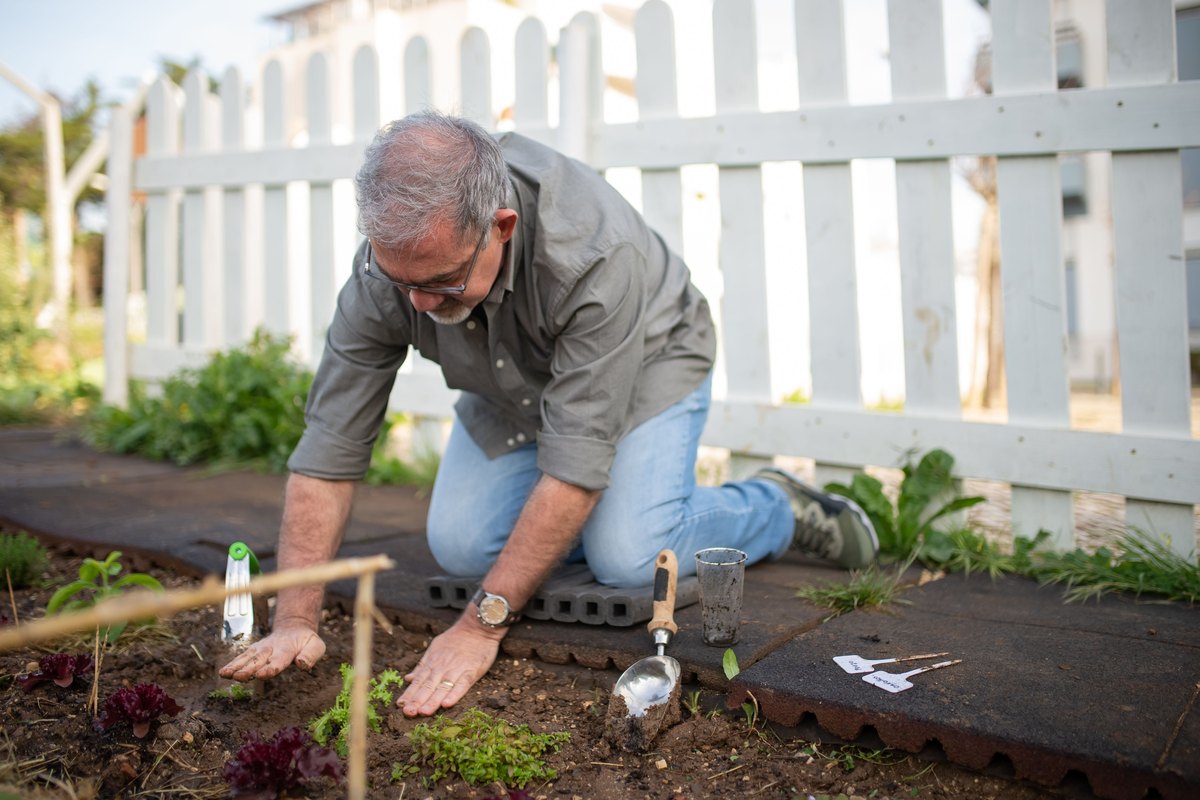 Man in glasses kneeling to plant seedlings in a garden bed