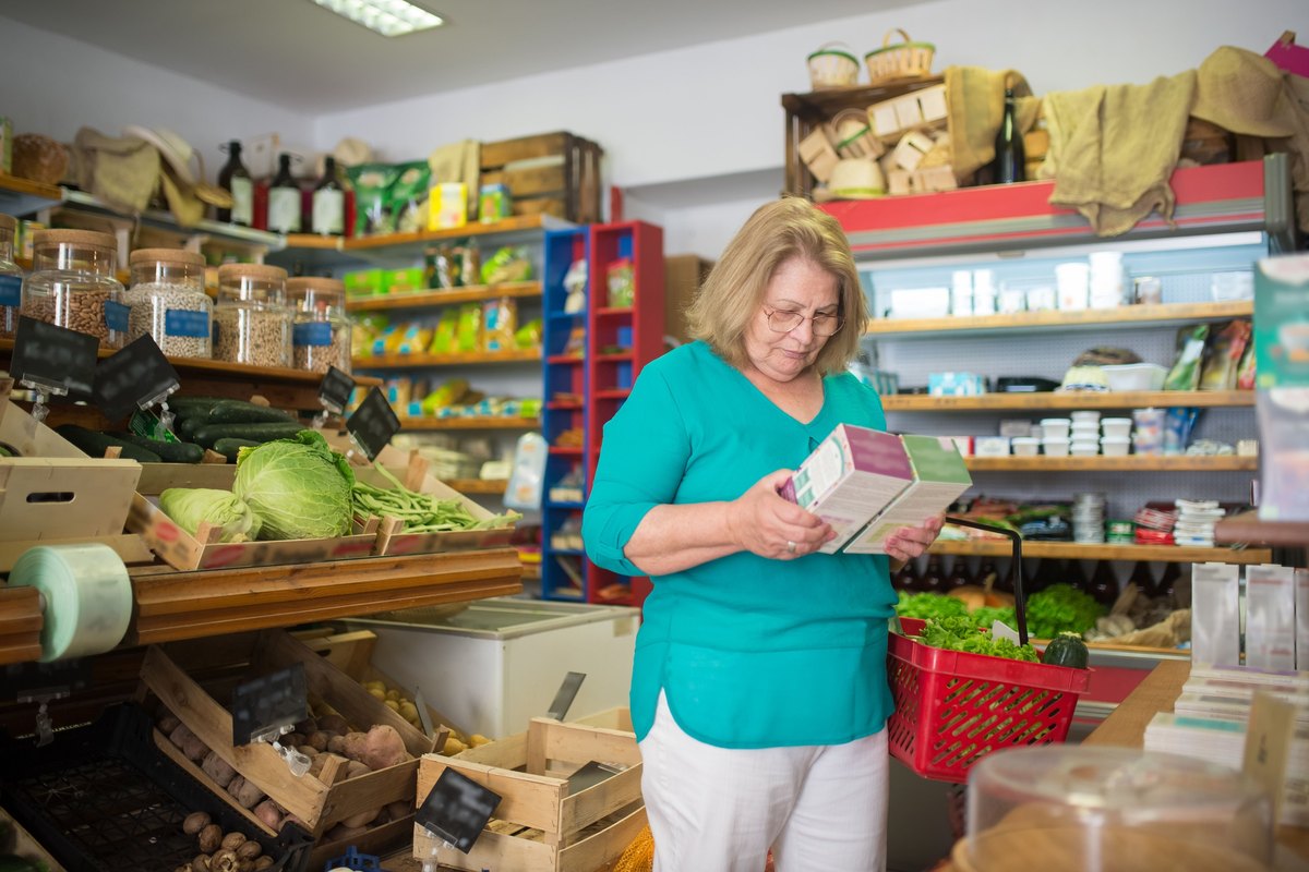Woman in glasses reading the back of a food box in a grocery shop
