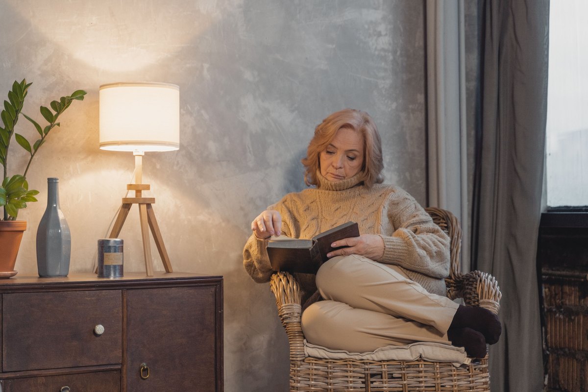 Woman in a cream sweater reading in a wicker armchair by a lamp