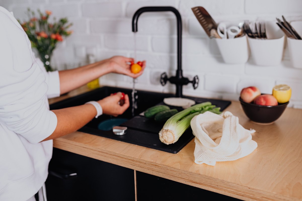 Person rinsing cherry tomatoes under a kitchen faucet beside celery