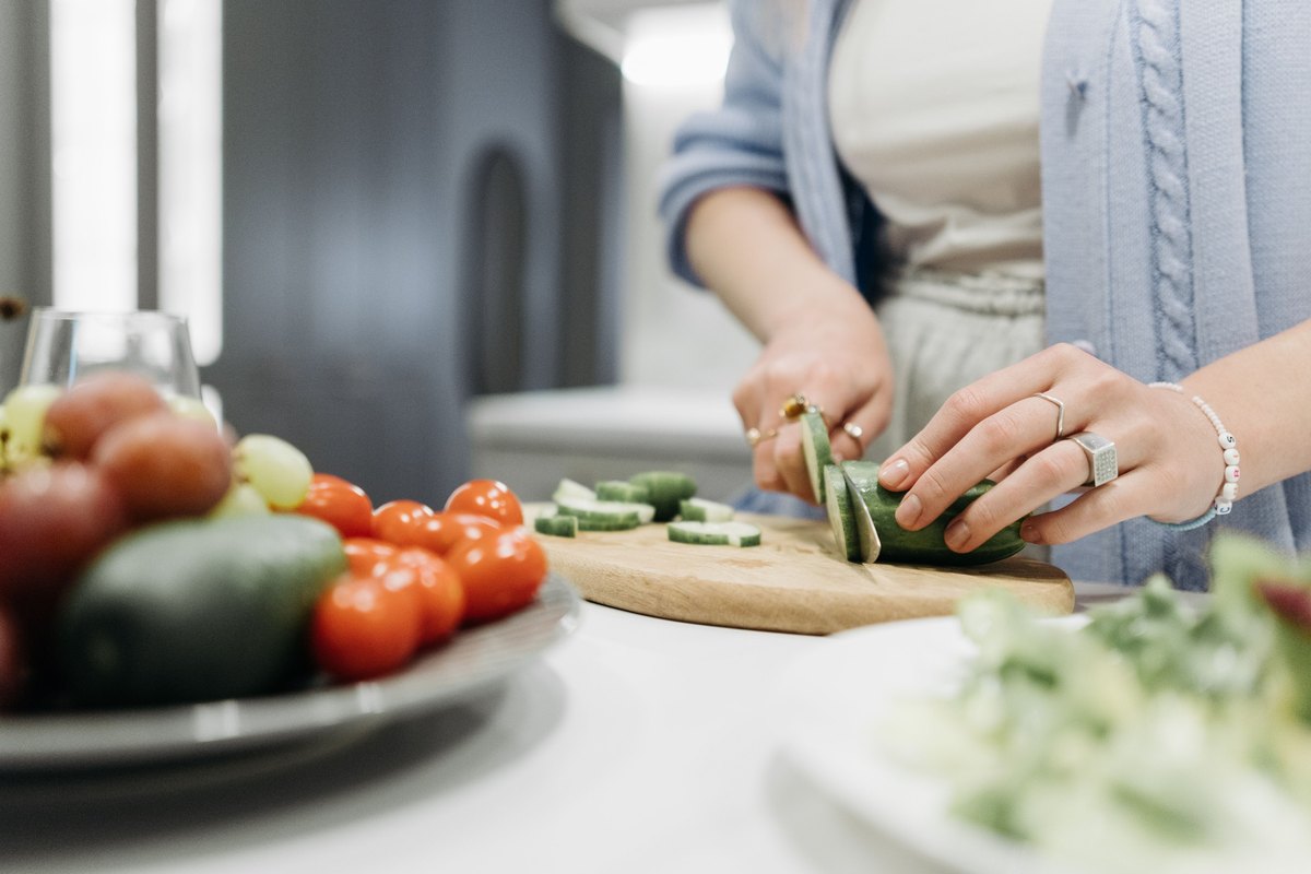 Hands slicing a cucumber beside a plate of cherry tomatoes