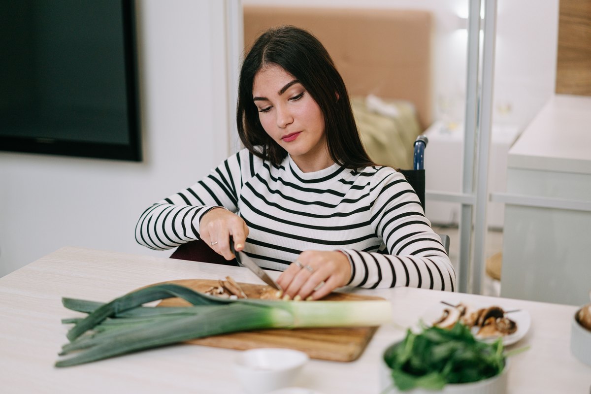 Woman in a striped top slicing mushrooms with a leek on the board