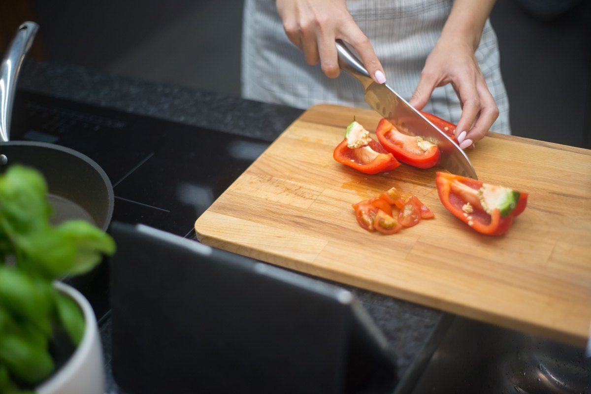 Hands slicing a red bell pepper on a wooden cutting board