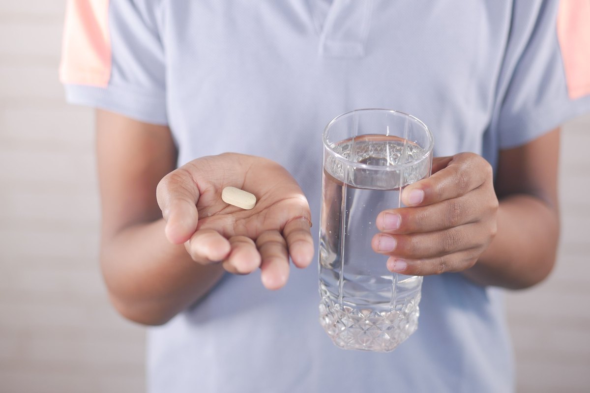 Hands holding a white tablet and a glass of water