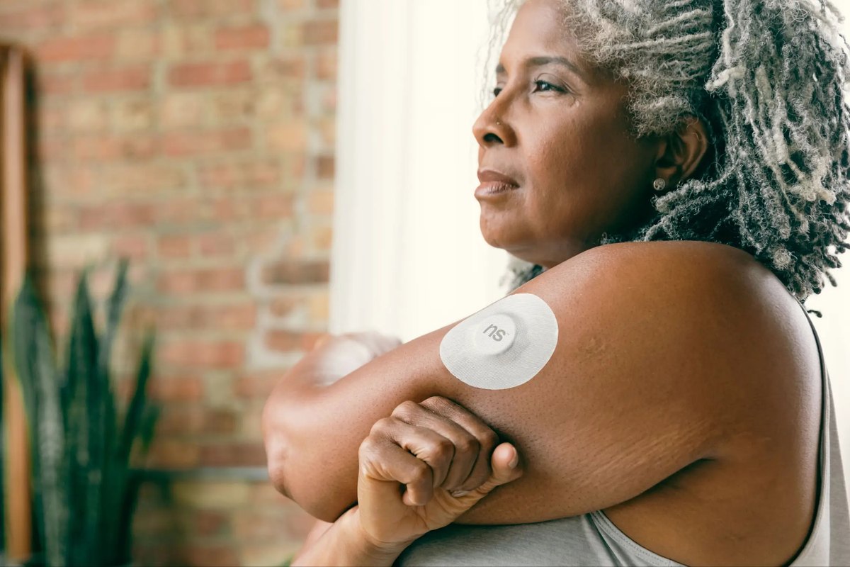 Woman at home with a glucose sensor patch on the back of her upper arm