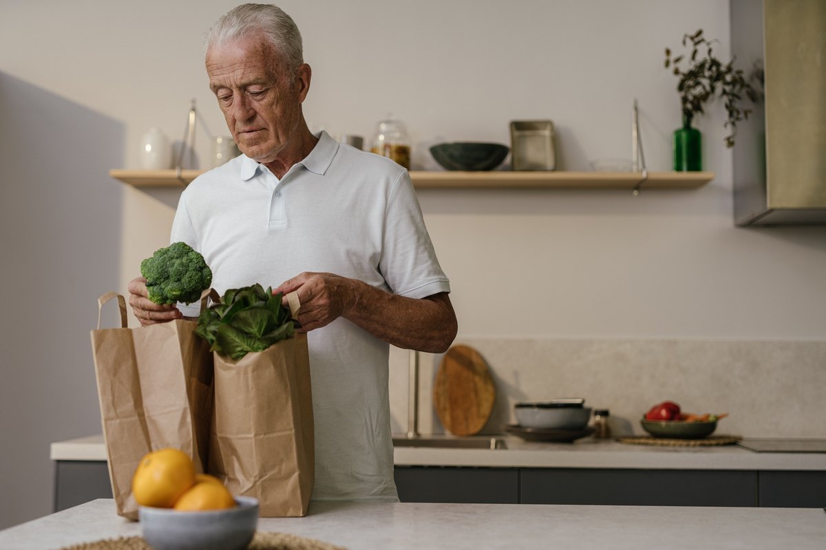 White-haired man unpacking broccoli and greens from grocery bags