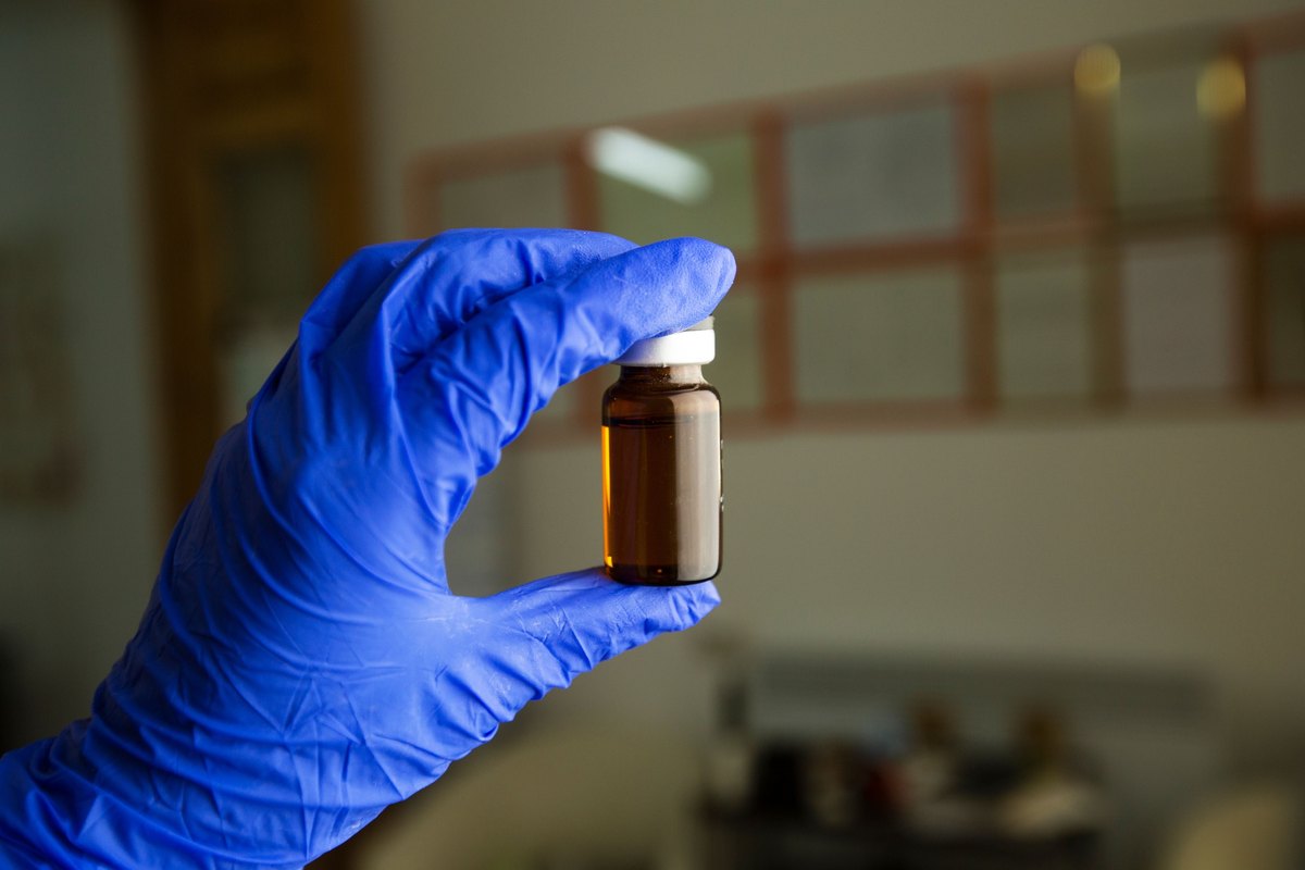 Gloved hand holding up a small amber glass vial