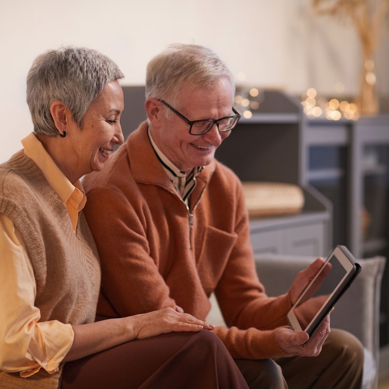 Older couple on a sofa smiling at a tablet