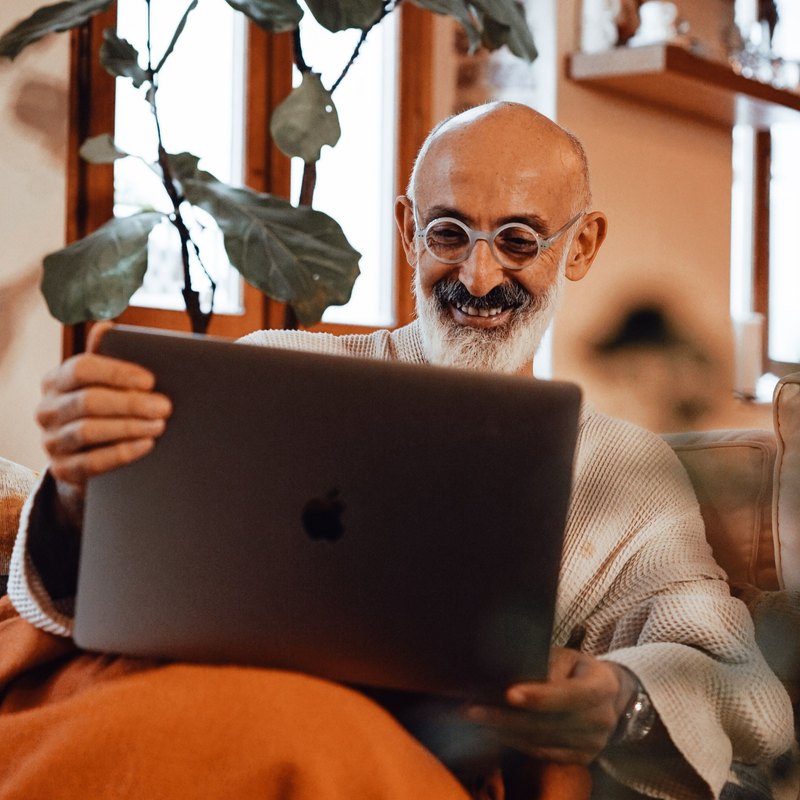 Bald man with a white beard grinning at a laptop on his lap