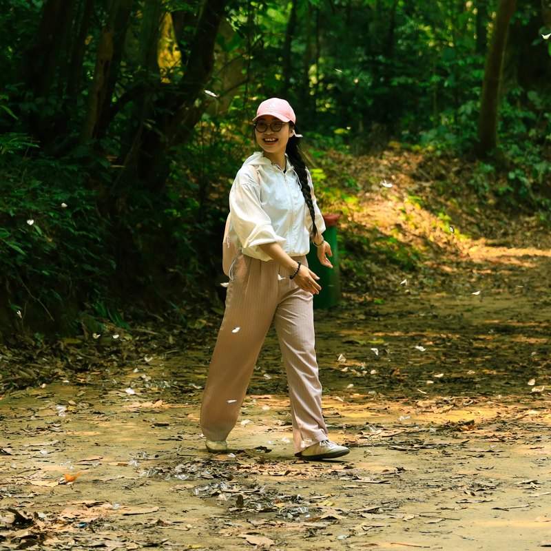 Smiling woman in a pink cap walking along a leafy forest road