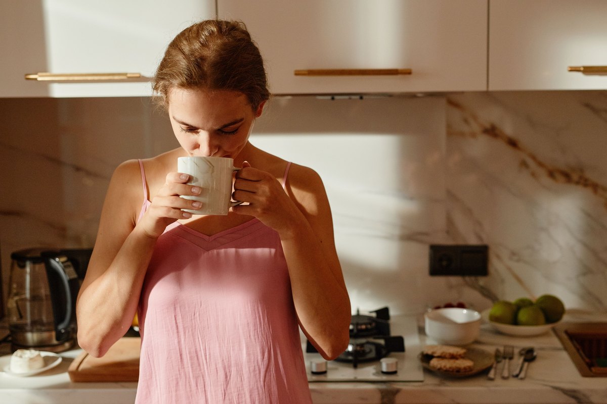 Woman sipping from a white mug in a sunlit kitchen