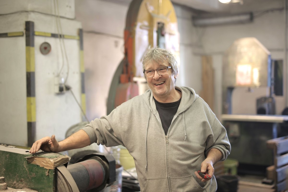 Smiling man in a gray hoodie at a workbench in a workshop